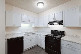 Kitchen with wood plank flooring, white cabinets and drawers, black appliances, and a semi-flush mounted ceiling light 