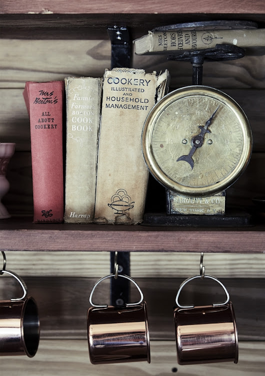 In the kitchen, copper mugs hang off wooden shelves below an antique scale.