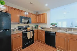 Kitchen with black appliances, wood floors, wood cabinets, overlooking into living room