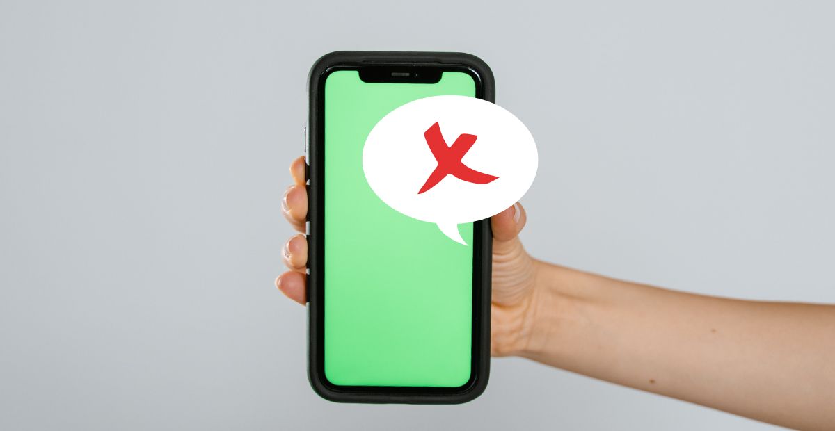 A light-skinned hand holding a phone with a green texting background and a text message bubble and a red mark of disapproval that Illustrates inappropriate messages to avoid sending during Ramadan.