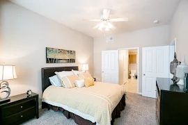 Fully furnished bedroom with ceiling fan, carpet, and white trim and doors