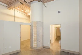 Bedroom with open door leading out to hallway, en suite bathroom, and cement accent wall feature with frosted glass