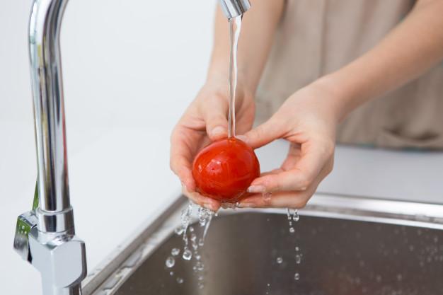 Woman washing tomato with tap water Free Photo