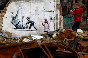 A girl stands next to graffiti of a child throwing a man on the floor in judo clothing on a destroyed building on November 14, 2022 in Borodyanka, Ukraine.  