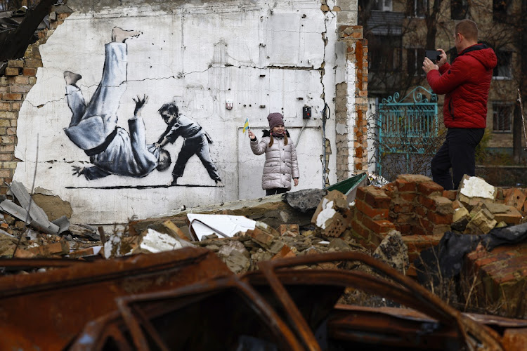 A girl stands next to graffiti of a child throwing a man on the floor in judo clothing on a destroyed building on November 14, 2022 in Borodyanka, Ukraine.