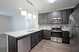 Kitchen with dark brown cabinets, granite countertops, stainless steel appliances, three pendant lights over sink, wood floors