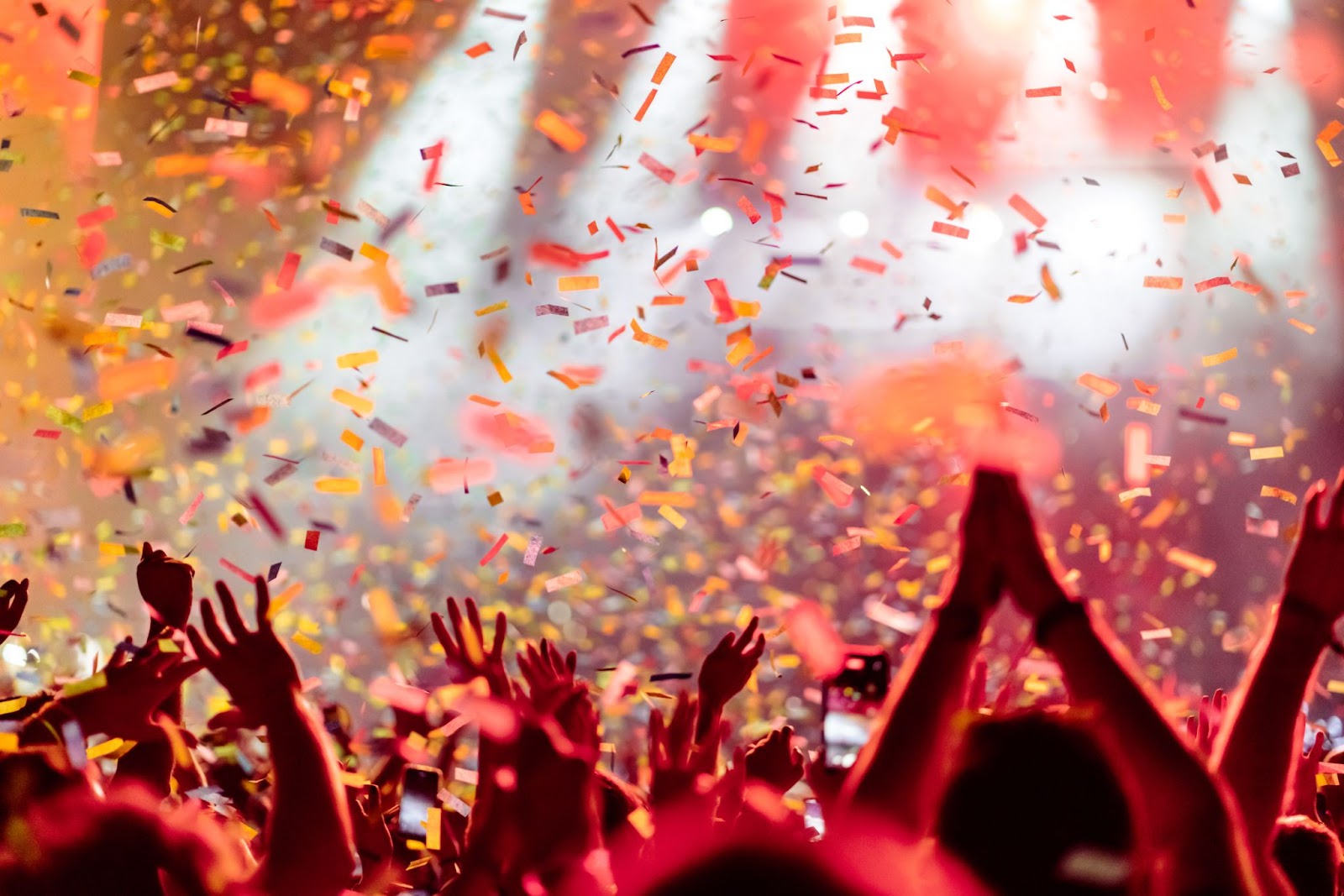 A bunch of fans at a concert with raised hands and confetti falling from the sky. 