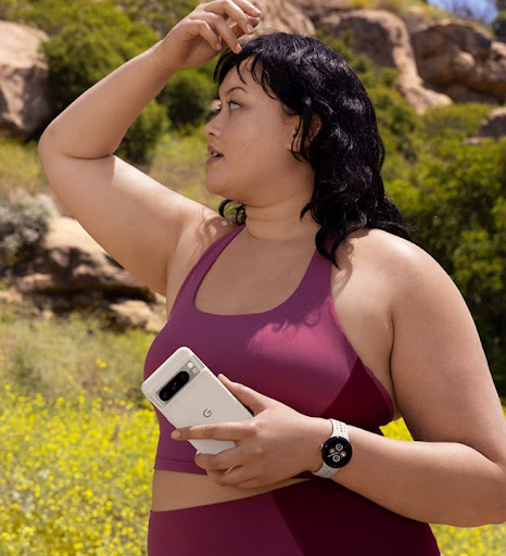 Une personne regarde autour d'elle sur un sentier de randonnée. Elle tient dans sa main gauche un Pixel 8 Pro doté d'une coque Pixel 8 Pro. Elle porte également une montre connectée Pixel.