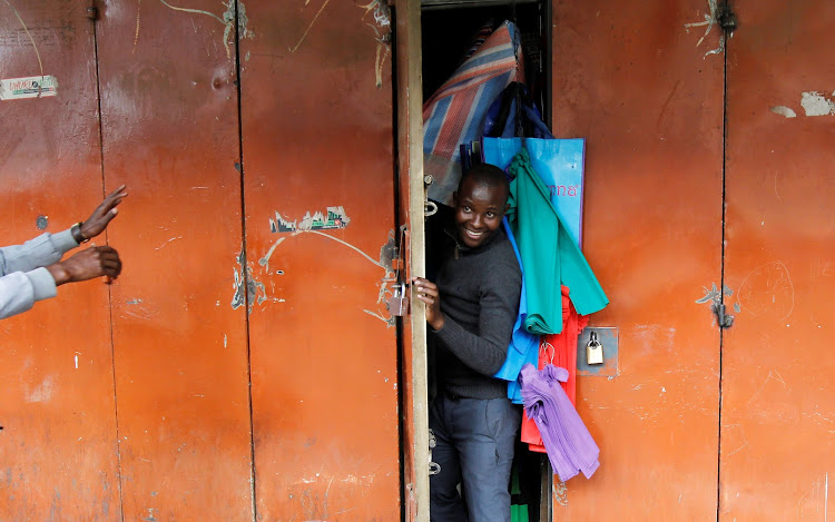 A resident peeps through the door of his shop as police patrol