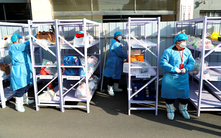 Workers wearing protective suits following the coronavirus disease (Covid-19) outbreak stand next to daily necessities placed on makeshift delivery racks, at a residential compound under lockdown after a case of the Omicron variant was detected, in Beijing's Haidian district, China January 18, 2022.