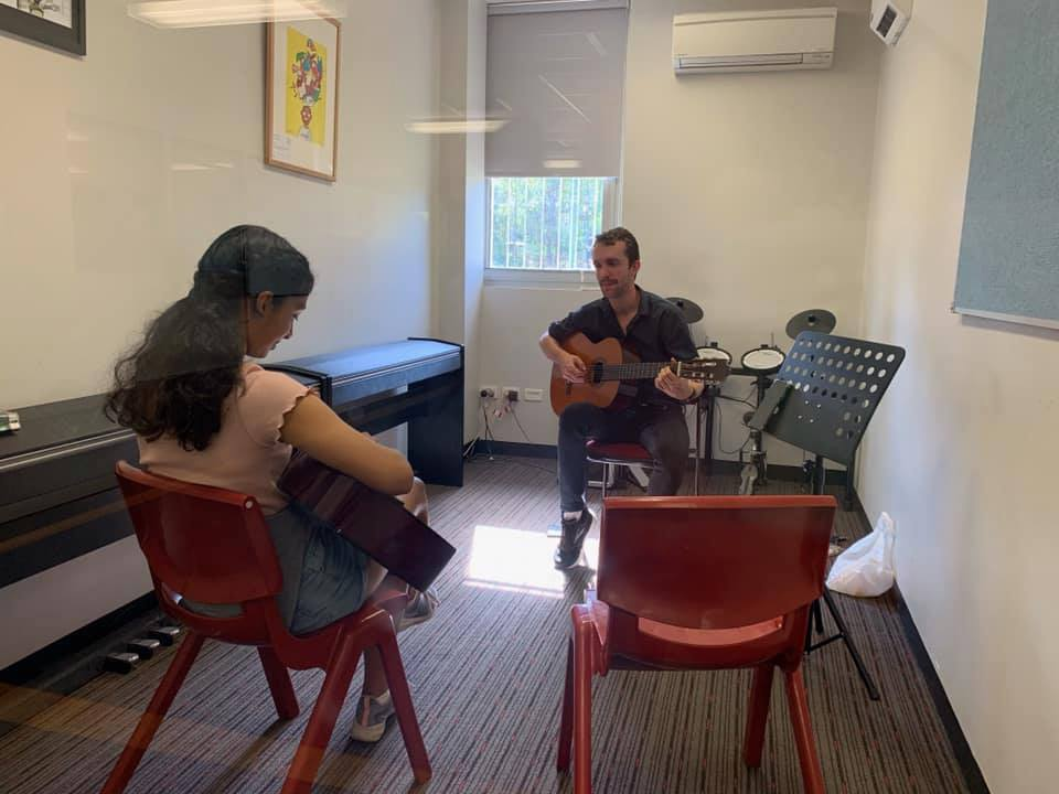 Student sitting with guitar tutor during an instrumental lesson. 