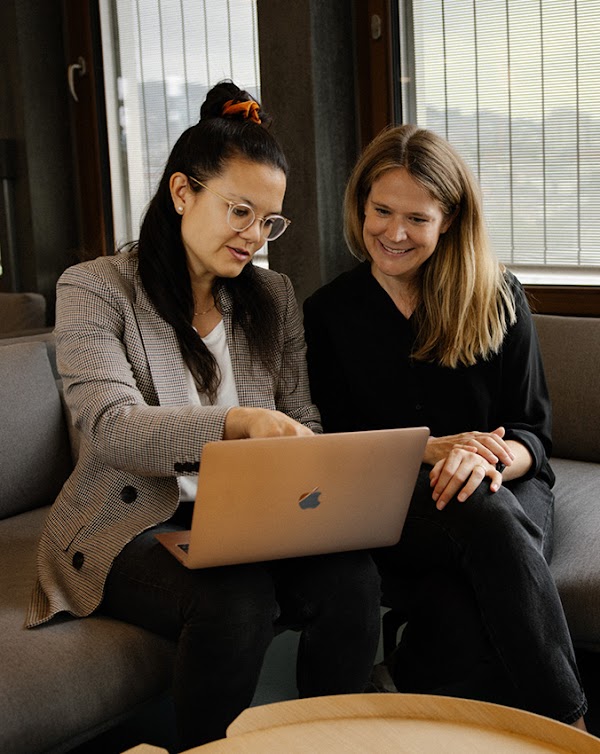 Anna Takihara et Jill Kümin, qui dirigent en tandem les relations publiques et la communication multimédia de Google à Zurich, sont assises sur un canapé.  Anna Takihara montre quelque chose sur l'écran de son ordinateur portable à Jill Kümin.