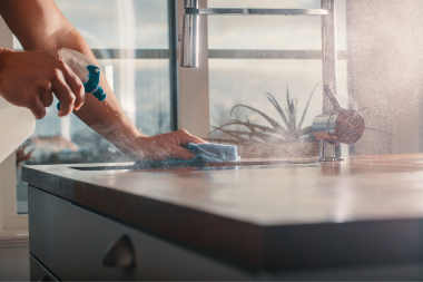 homeowner cleaning countertop of kitchen with spray bottle and rag custom built