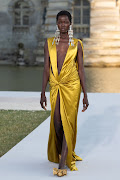 Model wears statement earrings paired with silky honeycomb yellow evening gown. 