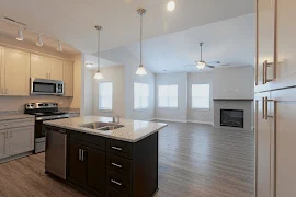 Large open concept living room and kitchen with kitchen island, several windows, fireplace, and wood plank floors