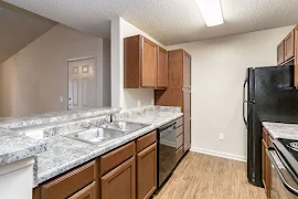 Gallery style kitchen with gray stone-inspired countertops, wood cabinets, and a breakfast bar overlooking the living room