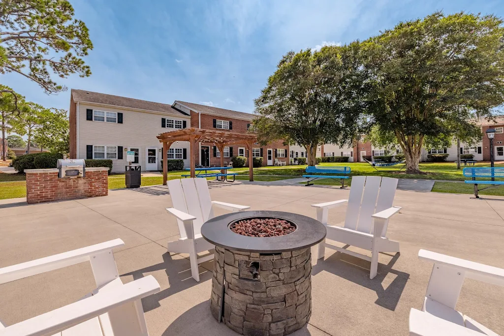Outdoor living area with a firepit on concrete patio, picnic tables, outdoor grill, & pergolas near the apartment buildings 