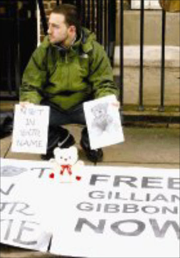 SUPPORTER: A protester holding placards and a teddy bear sits outside the Sudanese Embassy in London on Saturday., to protest the 15-day [rospm term given to British school teacher, Gillian Gibbons. Pic. Max Nash. 01/12/07. © AP.