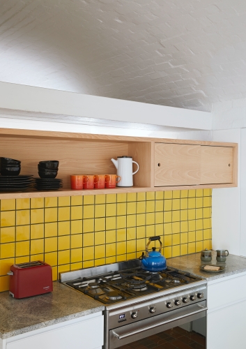 Bright-yellow tiles serve as a splashback, while adding a colour pop to this modernist kitchen.