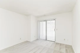 Corner of bedroom facing sliding glass patio door with vertical blinds on the far wall