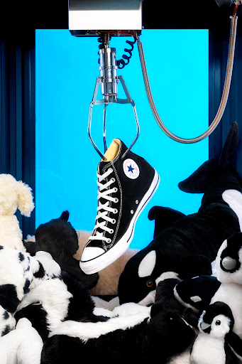 A claw machine grabbing a black Converse Chuck Taylor surrounded by black and white dolls.