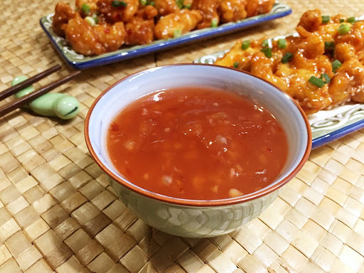 Some sweet chili sauce in a bowl with chicken bites in the background.