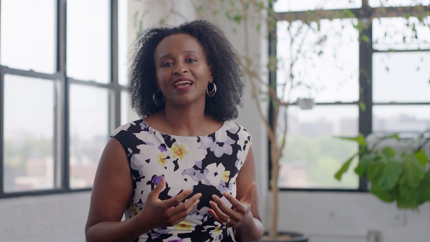 Still frame of Dr Tsedale Melaku from the waist up wearing a floral dress.