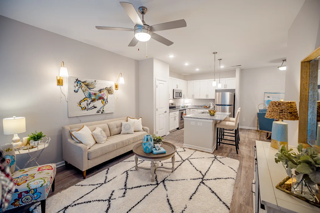 Furnished living room and kitchen areas with light gray walls, white trim, wood plank floors, and recessed lighting