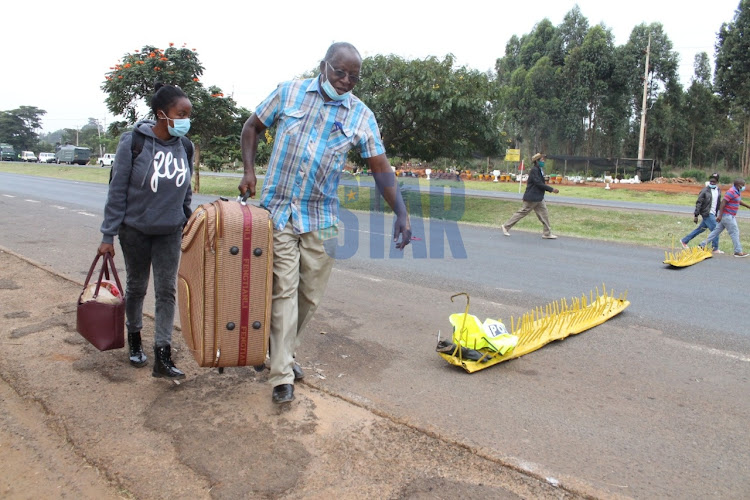 Travelers walk past a police roadblock at a checkpoint meant to indicate border of Kiambu and Murang'a counties in BluePost area, Thika on March 27, 2021