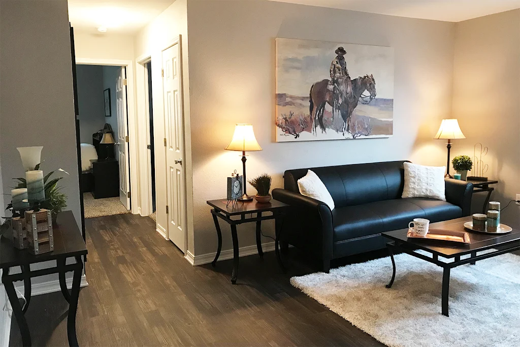 Furnished living room with wood-inspired flooring, beige walls, next to hallway leading to bedroom