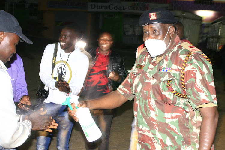 Baringo Central civil AP commander Ibrahim Abachilla offers to spray journalists’ hands with sanitiser during the curfew at Kabarnet town on Friday.