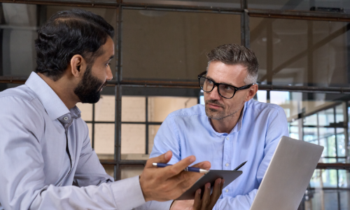 Two men in button up shirts in conversation with a laptop nearby.