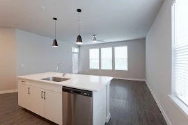 Modern apartment kitchen with white cabinets, stainless steel appliances, and pendant lighting over an island.