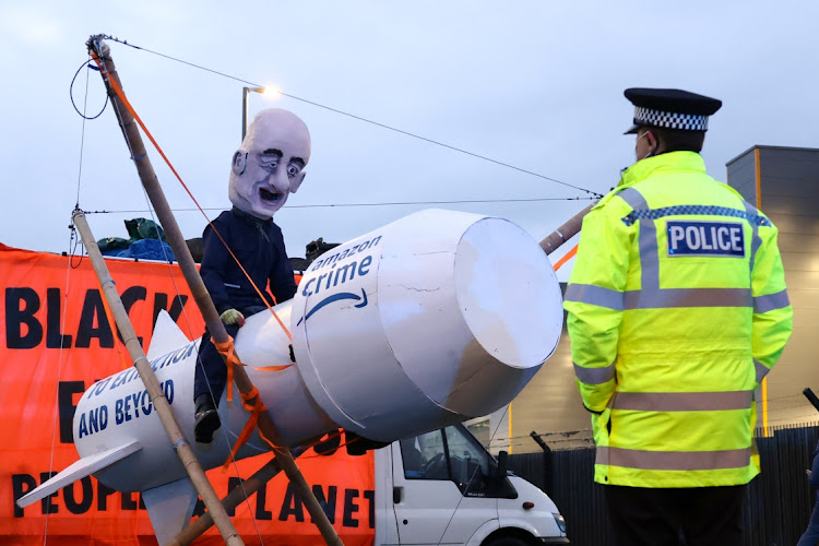 A police officer looks at a person wearing a head mask depicting Amazon founder, Jeff Bezos, as Extinction Rebellion activists block an entrance to an Amazon fulfilment centre in Tilbury, Essex, Britain, on November 26 2021. Picture: REUTERS/HENRY NICHOLLS