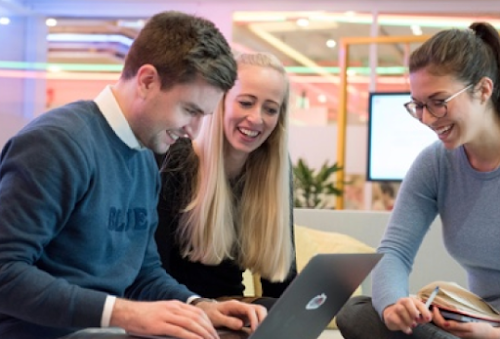 Three people gathered around a laptop, smiling.