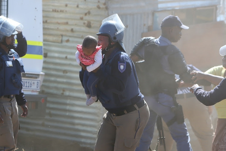 A Nelson Mandela Bay metro police officer takes the child to safety after her father threw her off the roof of a shack at the Joe Slovo informal settlement in Port Elizabeth on 12 April 2018.