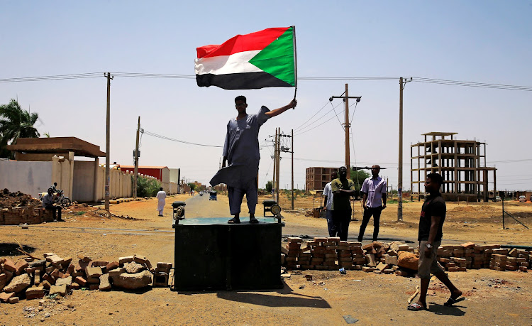 A Sudanese protester holds a national flag as he stands on a barricade along a street, demanding that the country's Transitional Military Council hand over power to civilians, in Khartoum, Sudan, on June 5 2019.