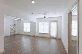 Living room with wood-inspired floors, large windows & a glass swing door with blinds, light walls & built-in shelves. 