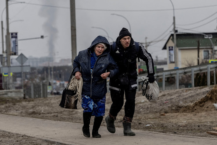 A man helps an elderly woman to run for cover after heavy shelling in Irpin, near Kyiv, Ukraine, March 6 2022. Picture: CARLOS BARRIA/REUTERS