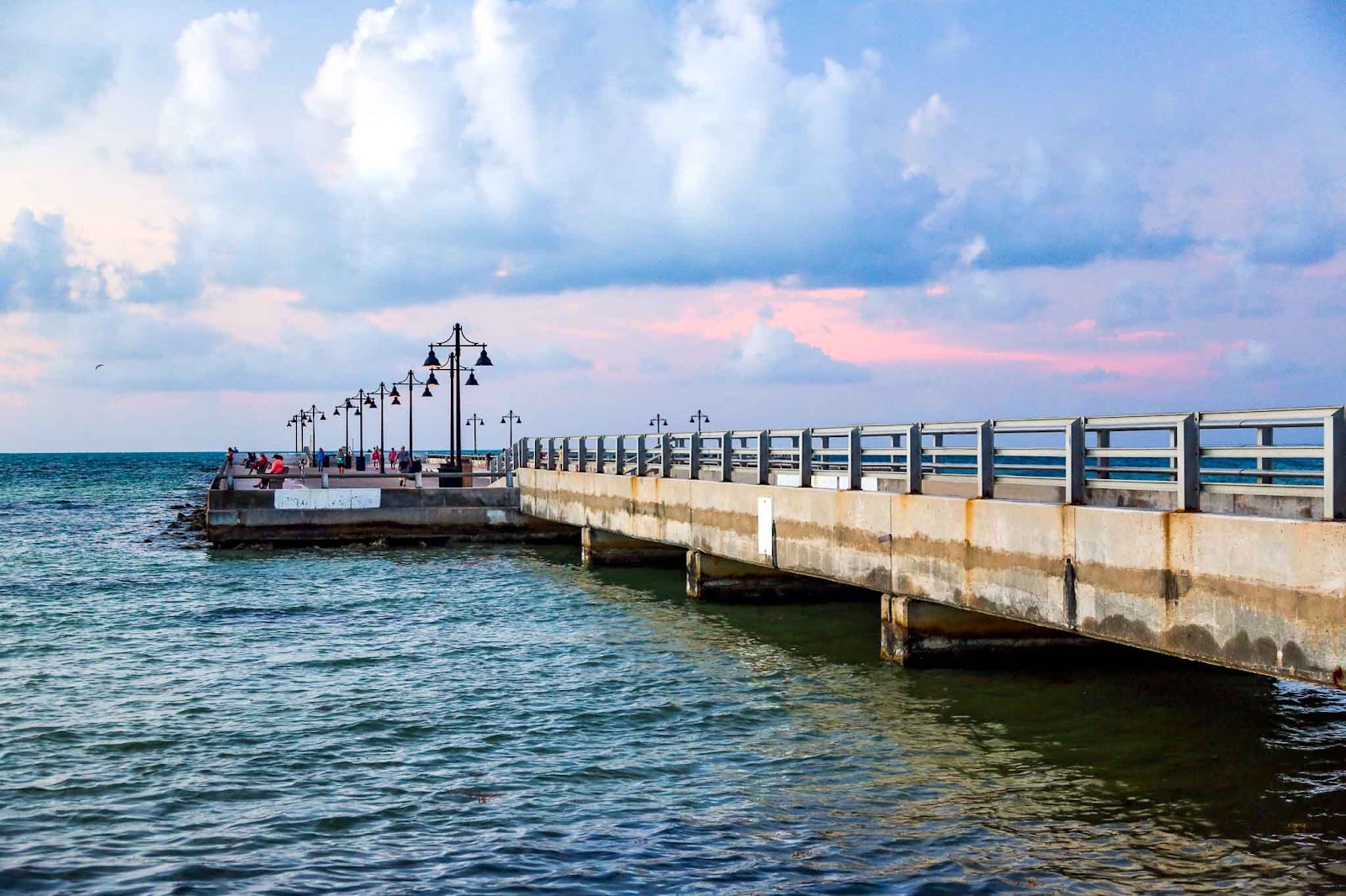 Edward B. Knight Pier juts out into incredible dark teal water. The sky in the background is filled with fluffy clouds and has a hint of pinky-orange in the middle.