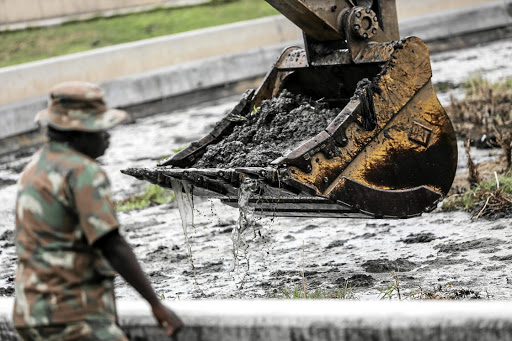 An army engineer directs an excavator clearing debris from a blocked section at a sewage treatment plant in the Vaal River system.