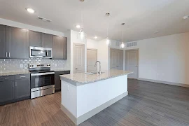 Kitchen with dark cabinets, stainless steel appliances, granite countertops, island with sink, wood floors into dining area