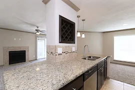 Kitchen island with built-in wine shelving, stone countertops, stainless steel appliances, and view of the fireplace