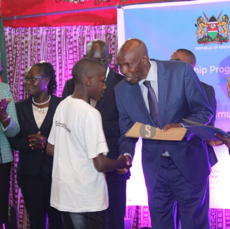 Education Cabinet Secretary Ezekiel Machogu awards a Busia learner, Laban Wafula a scholarship during the launch of the 2024 Elimu scholarship program at the Bomas of Kenya, Nairobi on January 19, 2023