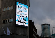 A Covid-19 message on a building in central Birmingham, U.K.. The advert in question however showed four households - one in which a woman holds a baby next to what seems to be an ironing board, another with a woman home-schooling two children, and a third with two women who are cleaning.