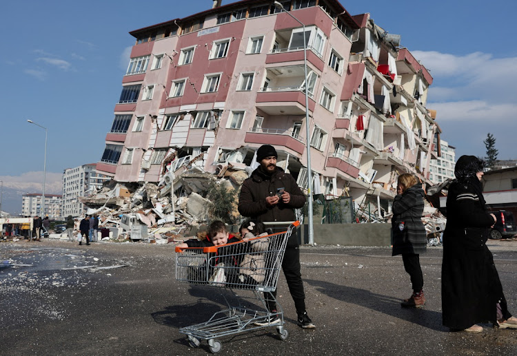 Children sit in a shopping cart near a collapsed building in Hatay, Turkey.