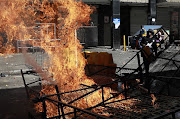 A foreign national adds flames to a fire in the CBD, after a foreign owned shop was looted. The foreign community gathered weapons for protection.