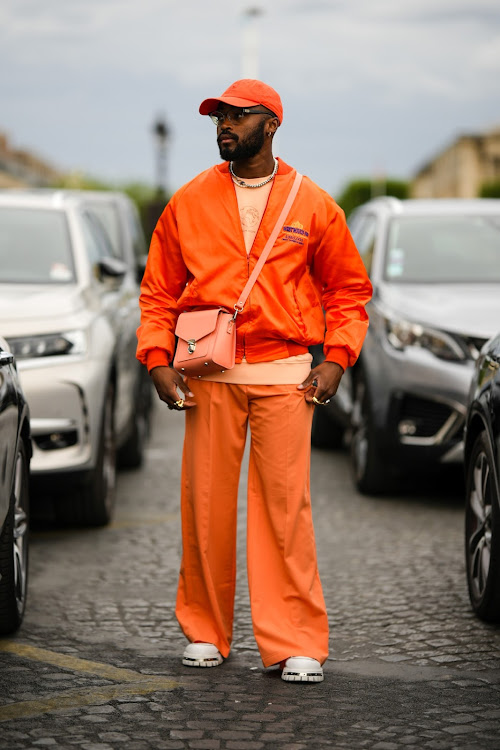 A guest wears an orange cap from Converse, a pale orange embroidered sweater from Thom Browne and a neon orange zipper oversized bomber coat outside the Thom Browne show during Paris Fashion Week - Menswear Spring/Summer 2023.