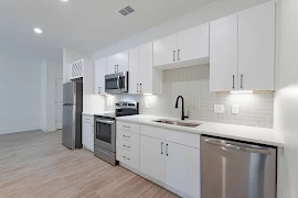 Modern kitchen in apartment with stainless steel appliances, white cabinets, and subway tile backsplash.