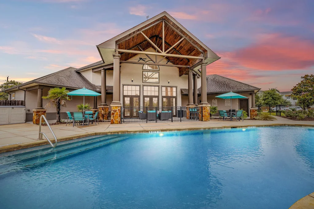 Resort-style swimming pool at dusk with lounge chairs on the pool deck and view of the clubhouse